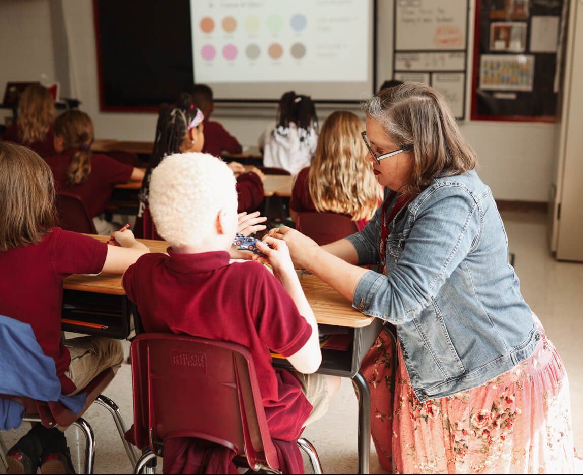 A teacher kneels down at a students desk to communicate with them