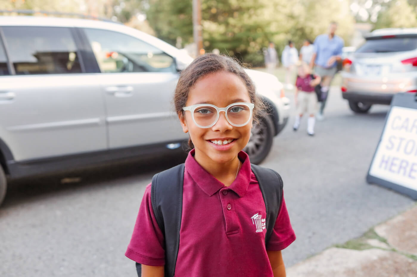 Student looks at camera and smiles in parking lot as students arrive to school